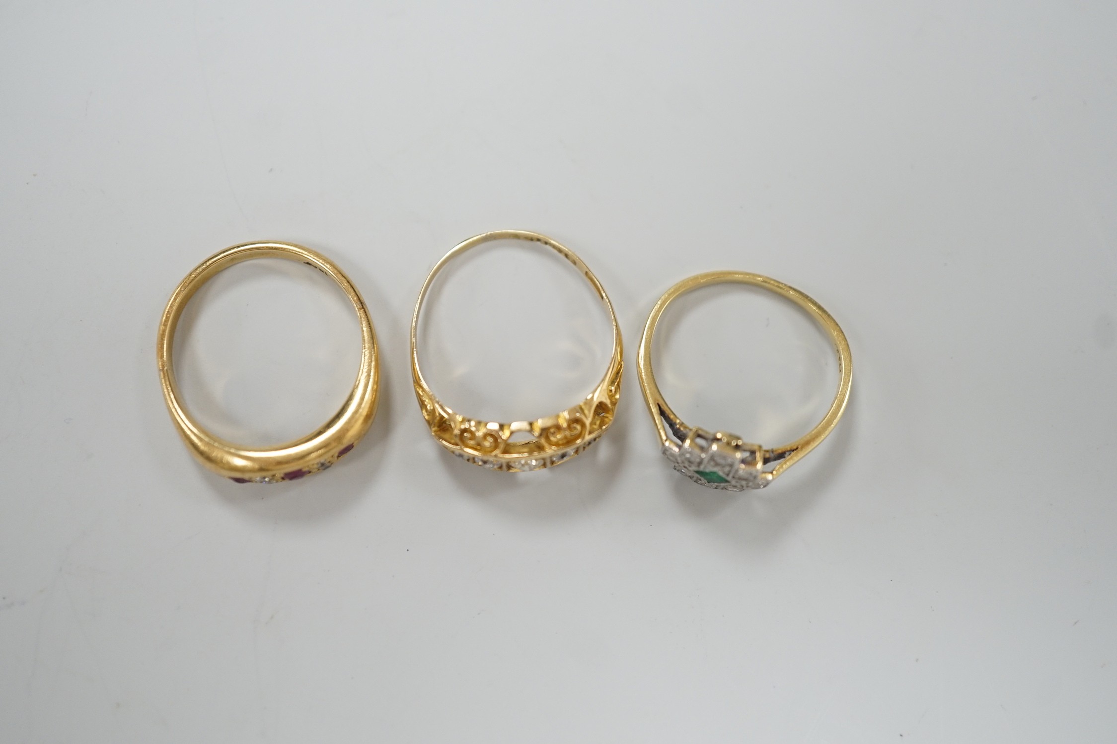 Three early 20th century 18ct and gem set rings, including ruby and diamond chip, size O, graduated five stone diamond, size P and an emerald and diamond cluster, size M, gross weight 10 grams.